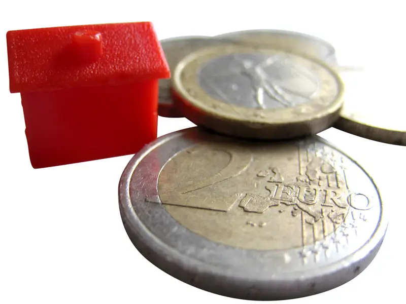 Rood modelhuisje naast euromunten als symbool voor subsidie op woningisolatie